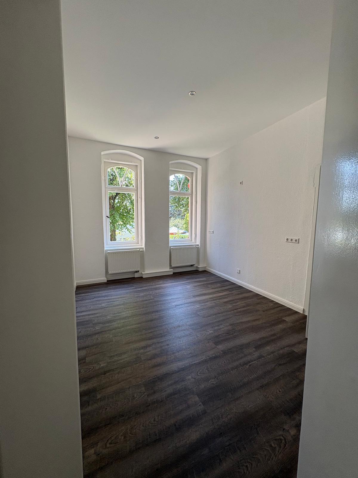 Fertig renovierter heller Altbauraum mit dunklem Boden und zwei Fenstern
