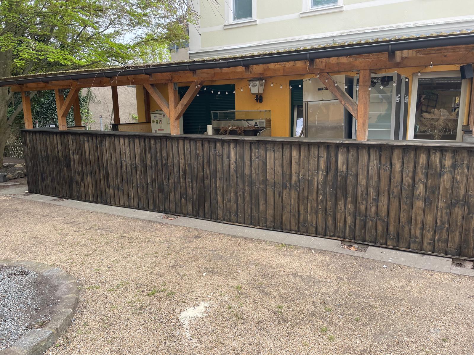 Fertiggestellte lange Außenfront mit dunkler Holzverkleidung unter einem Holzdach
