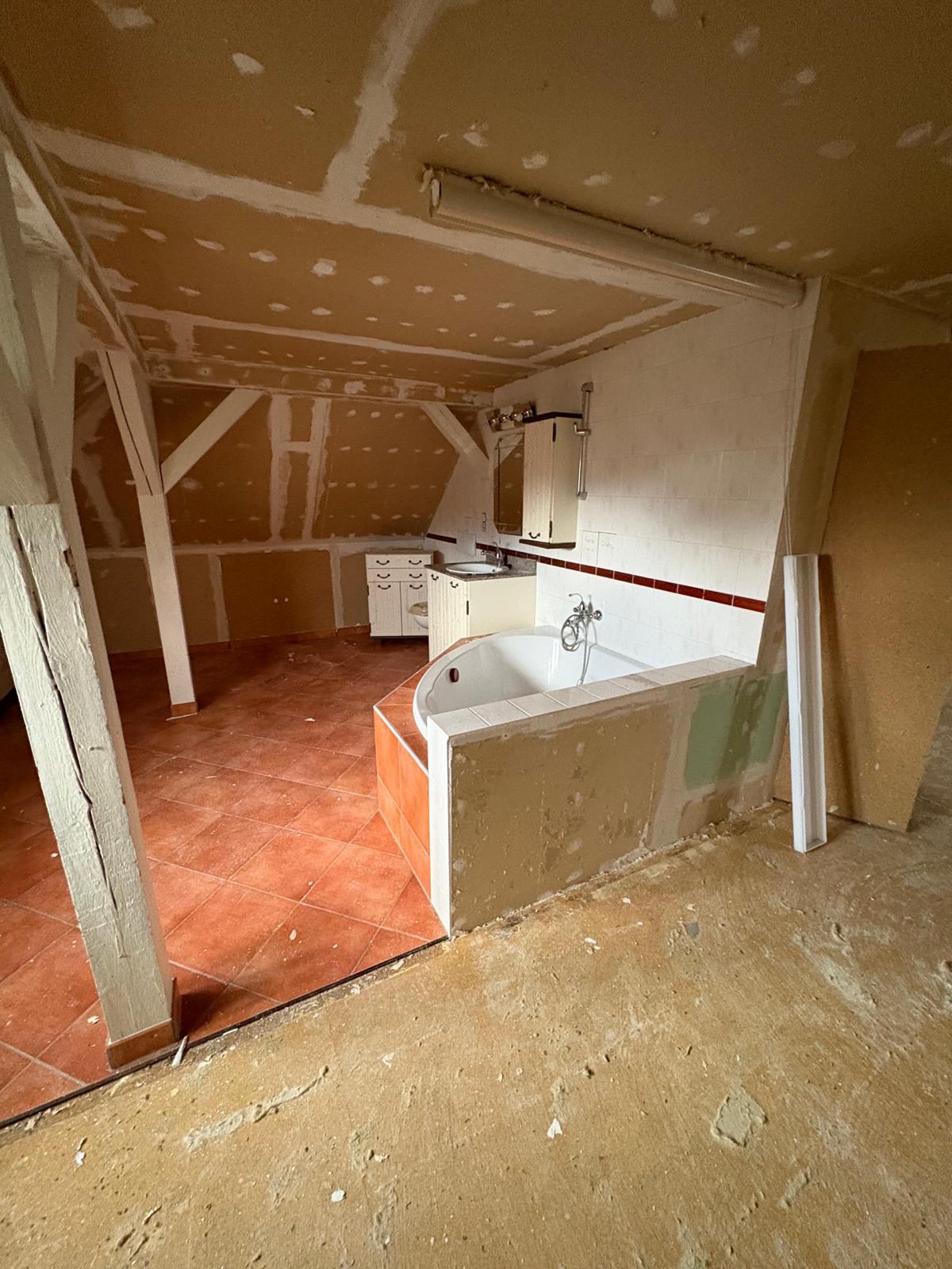 Älteres Dachgeschossbad mit Badewanne, kleinteiligen Fliesen und offenen Trockenbauflächen