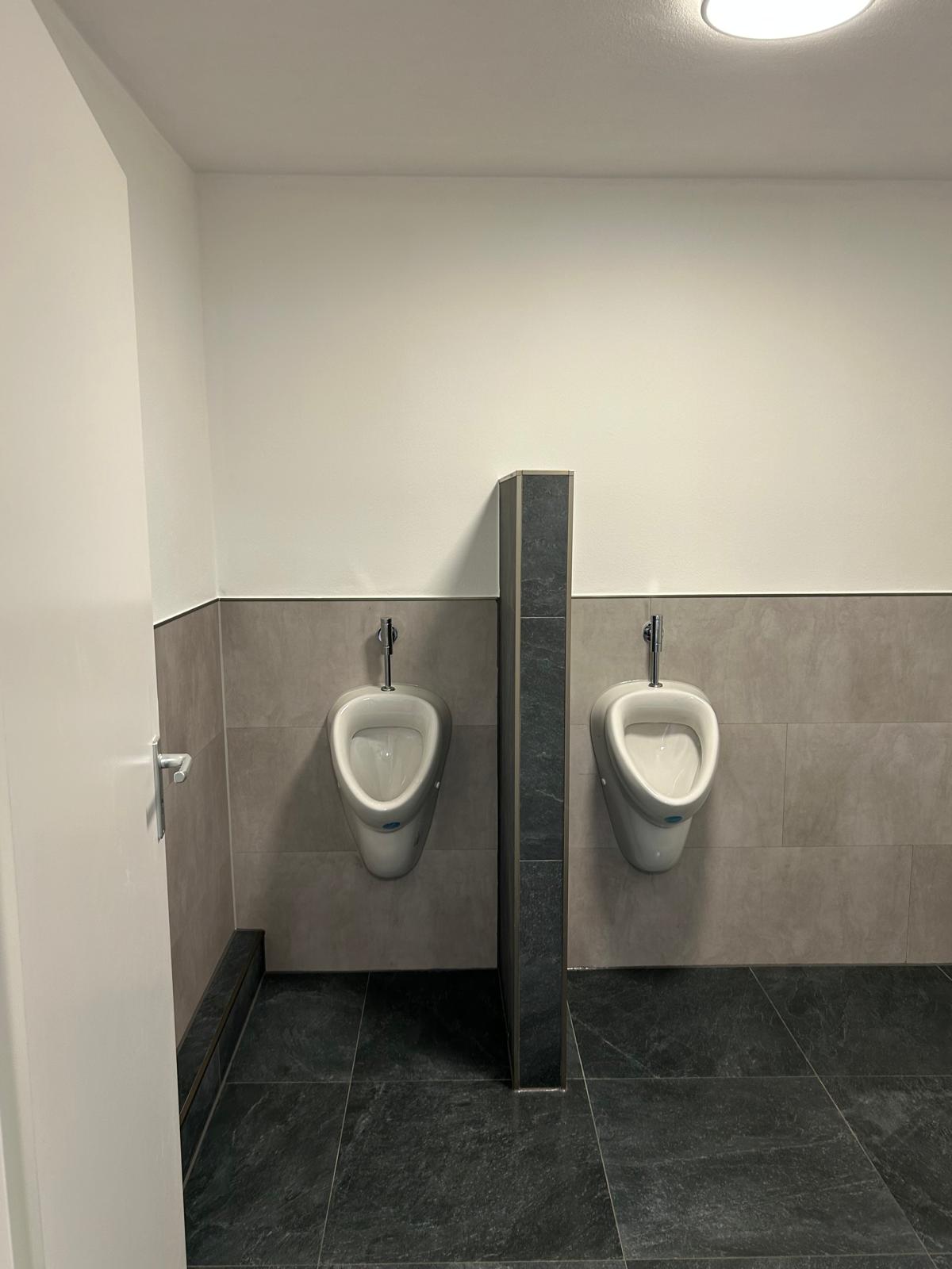 Fertig gefliester Urinalbereich mit zwei Urinalen und Trennwand