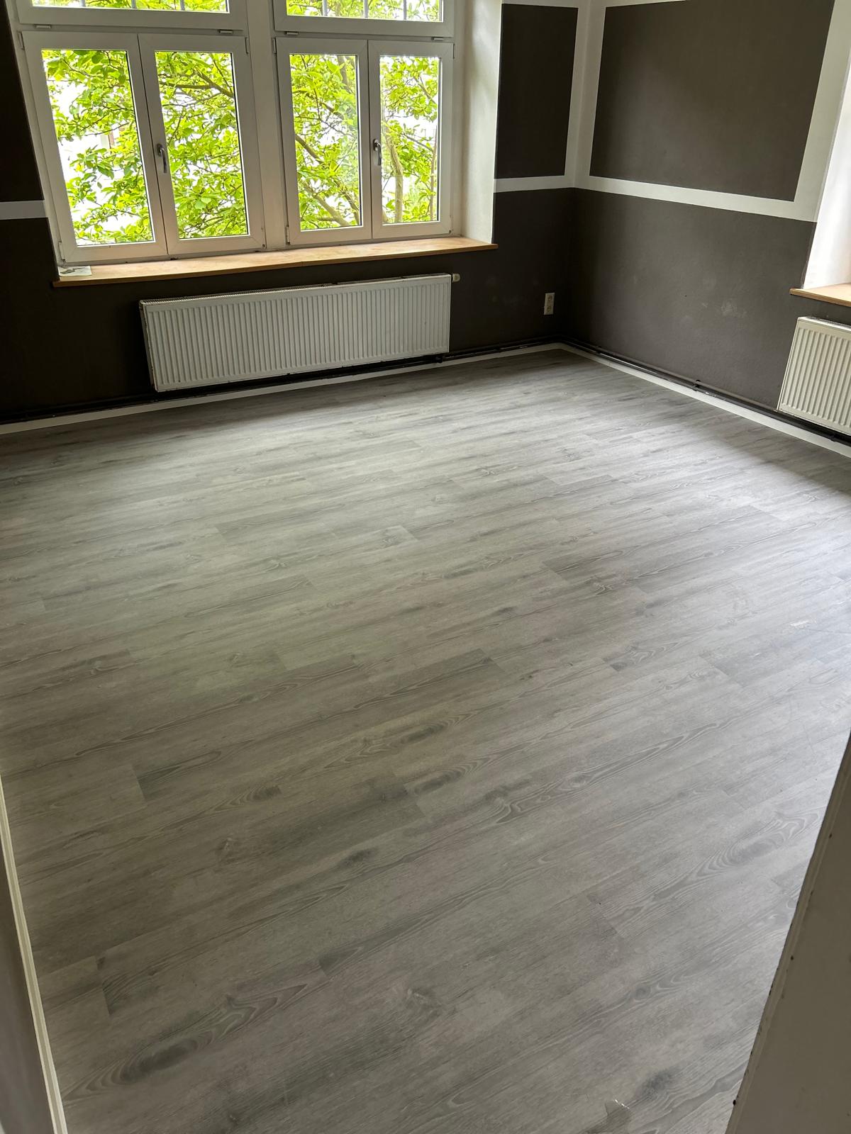 Wohnraum mit hellem grauem Vinylboden und dunklen Wandflächen